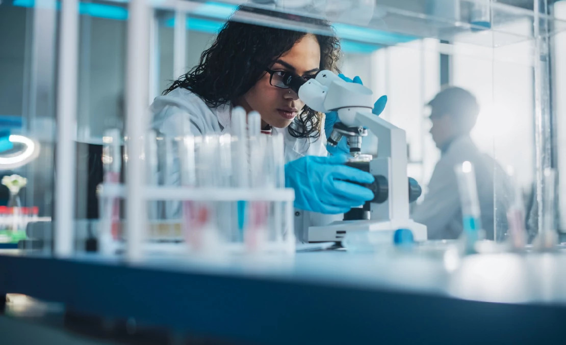 woman looking through microscope in a lab woman looking through microscope in a lab